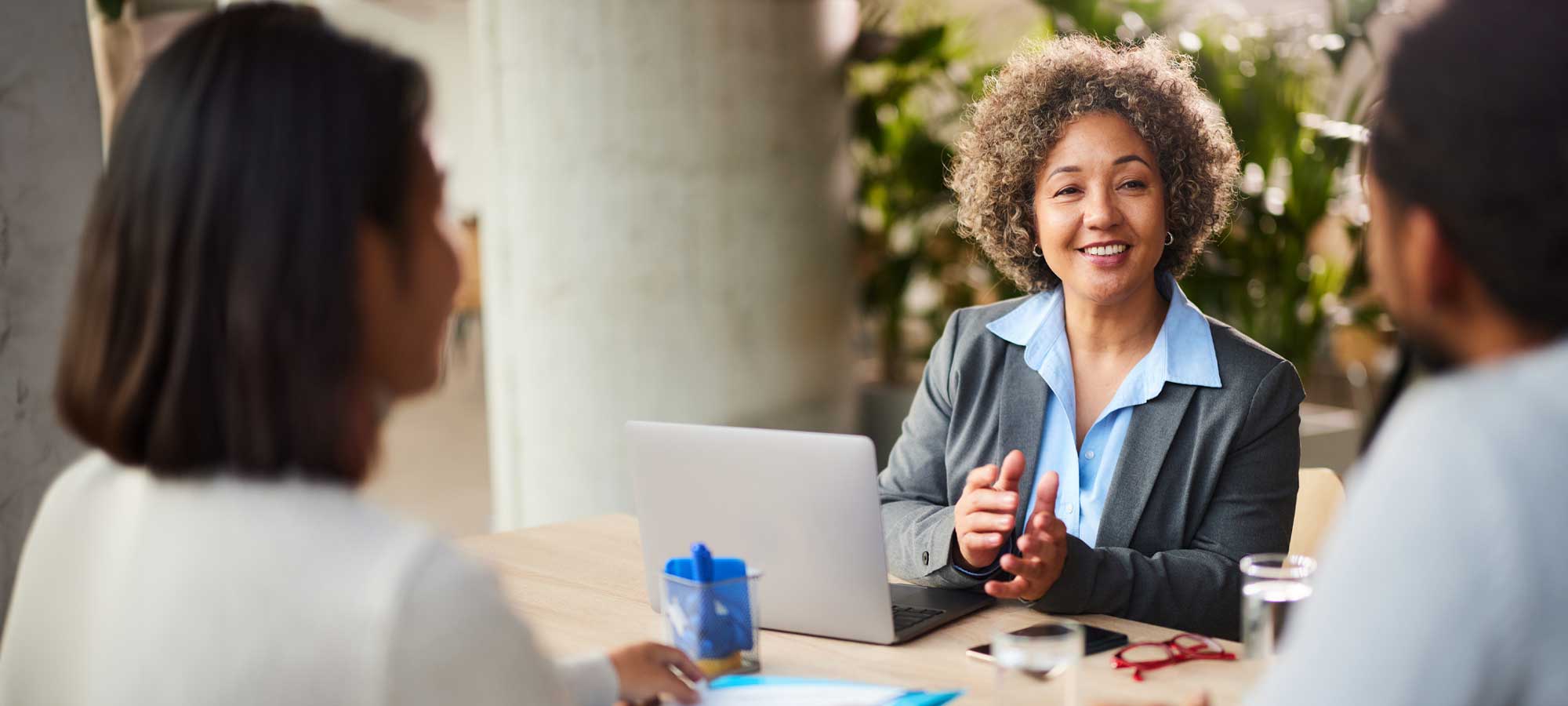 A Citizen First Bank Corp financial advisor with short curly hair is smiling and gesturing while seated at a table with her computer. She is meeting with a client to discuss their financial needs, symbolizing the expert and personalized service we offer.